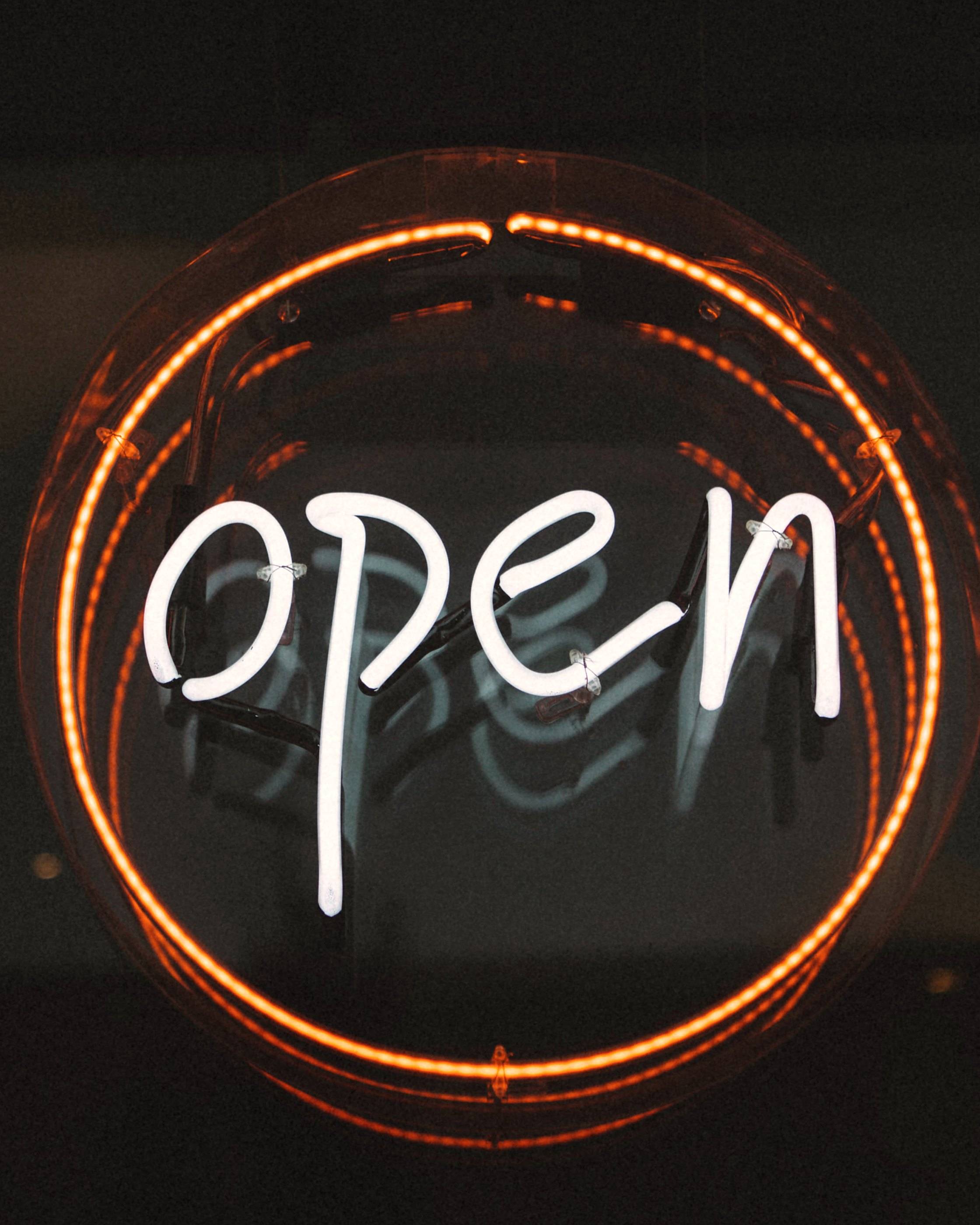 A round neon sign reading "open" glowing in a dark shop window